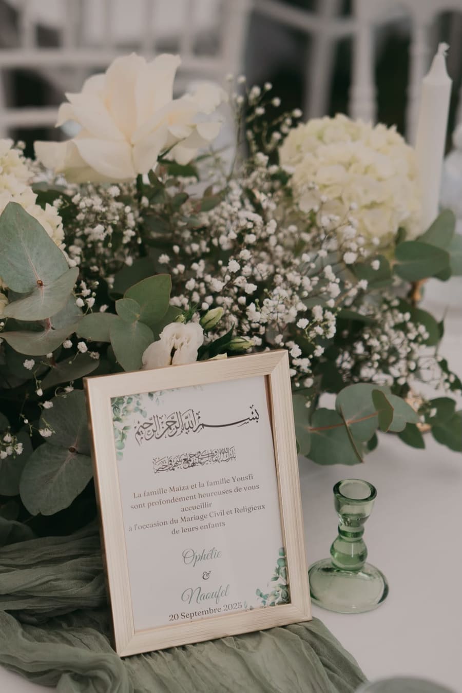 Cadre de bienvenue calligraphié posé devant une composition de roses blanches, gypsophile et eucalyptus