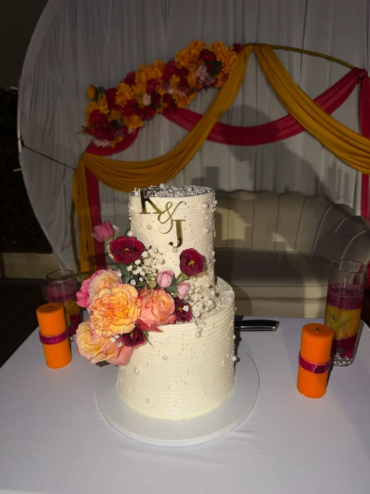 Gâteau de mariage à deux étages, perles de sucre et cascade de fleurs fraîches devant une arche drapée